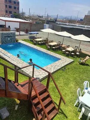 two people in a swimming pool with tables and umbrellas at casa de playa en lurin con piscina y parrilla in La Planicie