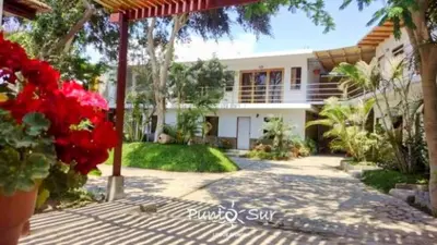 a large white house with red flowers in front of it at Punto Sur Lodge - Chincha in Chincha Alta