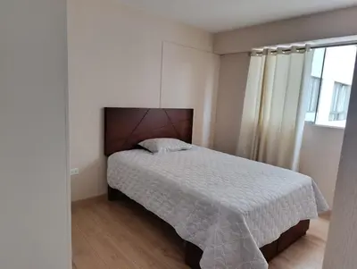 a bedroom with a bed with a white comforter and a window at Tu mejor opción Departamento Familiar in Lima