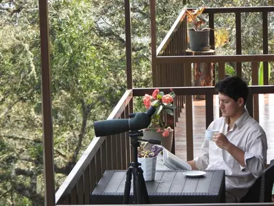 a man sitting at a table on a deck with a camera at Ecoterra Inka Lodge in Quillabamba