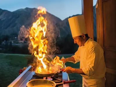 a man cooking food on a grill with flames at Inkaterra Hacienda Urubamba in Urubamba