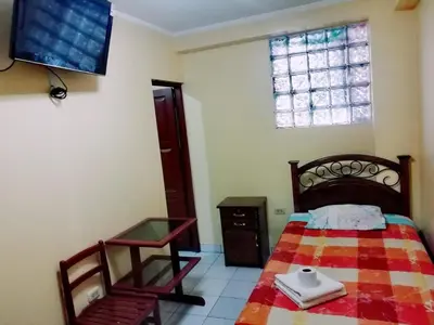 a bedroom with a bed and a chair and a tv at Hs San Cristobal in Ayacucho