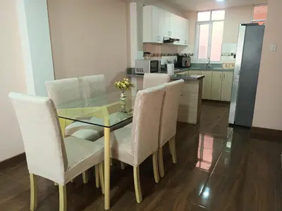 a dining room table with white chairs and a kitchen at Katty's apartment - Las Malvas in Lima