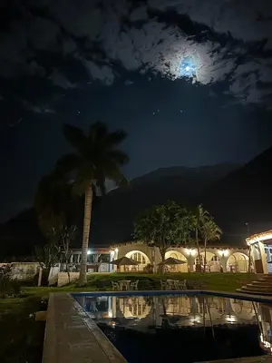 a night view of a pool with a palm tree and the moon at QPÑ Hoteles - Hacienda Nieve Nieve in Balconcillo de Aviyay