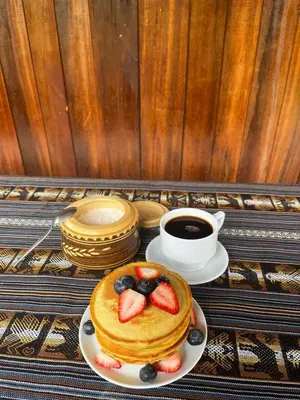 a plate of pancakes with strawberries and blueberries and a cup of coffee at ALPHINA CABINS Qhapaq Ñan in Sahuayacu