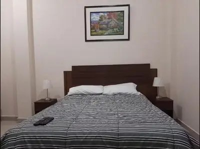 a bed in a bedroom with two lamps and a picture at Habitación privada cerca a la plaza Constitución en un 1er piso in Huancayo