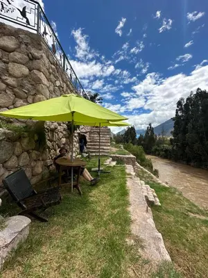 a table with a green umbrella next to a river at Yoga Home in Urubamba