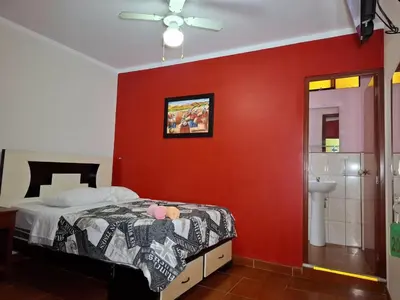 a bedroom with a red wall with a bed and a toilet at Hostal los Faroles in Barranca