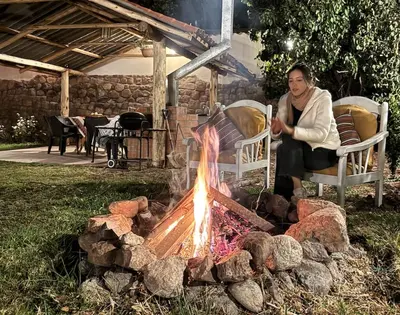 a woman sitting in a chair next to a fire at Urquillos Wasi - Andean Cottage in Urubamba