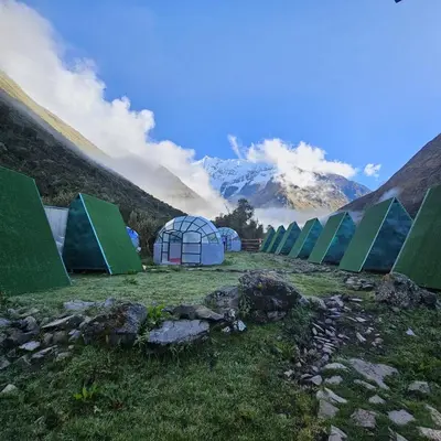 a row of green tents in a field with mountains at Salkantay starcamp in Anta