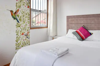 a white bed with a pink pillow and a window at Apart Hotel El Puma in Cusco