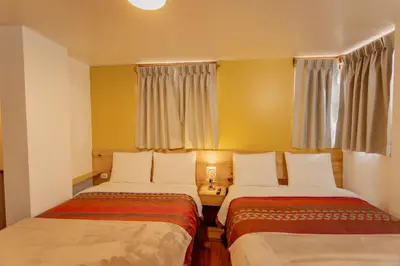 two beds in a room with yellow walls and windows at Kamma Guest House in Ollantaytambo