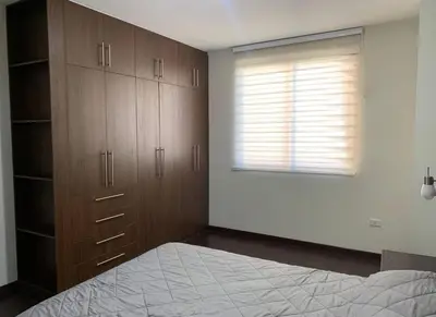 a bedroom with a bed and wooden cabinets and a window at Los Tambos Apartment in Cusco