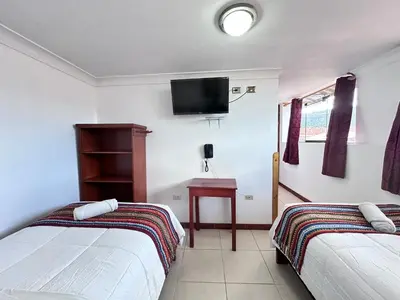 a bedroom with two beds and a tv on the wall at Libertrek in Cusco
