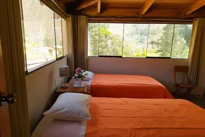 two beds in a room with two windows and a table with flowers at Tambo de Ollantay Hotel in Ollantaytambo
