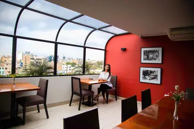 a woman sitting at a table in a restaurant with a window at Palmetto Hotel Business La Perla in Lima