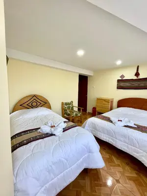 two beds in a hotel room with white sheets at TORIBIANS Hotel in Chinchero