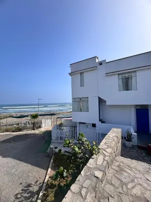 a white house with a stone wall next to the beach at Departamento en Chancay con Vista al Mar y cerca al Megapuerto