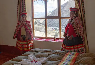 two women standing next to a bed in front of a window at hotel turismo vivencial pallay lliclla in Urubamba