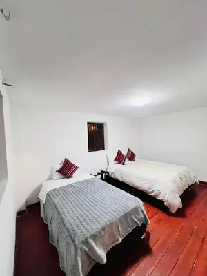 two beds in a room with white walls and wooden floors at SkyGuest Cusco San Cristobal in Cusco