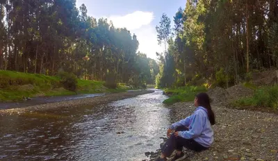 a woman sitting on the rocks by a river at Fundo Venegas & Montoya in Jauja