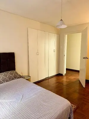 a bedroom with a bed and white cabinets and wood floors at Miraflores, habitación en apartamento compartido in Lima