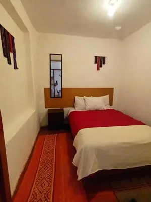 a bedroom with a bed with a red blanket and a mirror at Yuraq Wasicha in Cusco
