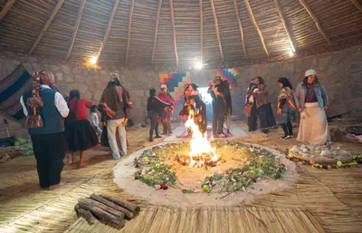 a group of people standing around a fire in a room at Pachamama Hampina Wasi Ancestral Center in Urubamba