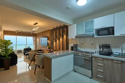 a kitchen with a counter top and a living room at Apartamento moderno cerca del Parque Wallenberg in Lima