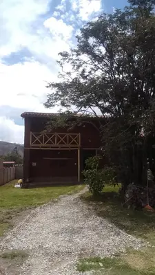 a brown building with a tree next to a gravel road at Casa tarawasy hostel in Urubamba