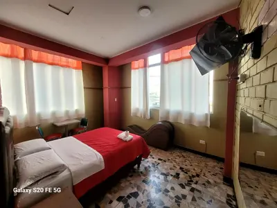 a bedroom with a bed with a red blanket and windows at Las Estrellas Hostal in Puente Piedra