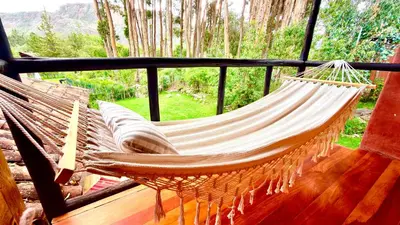 a hammock on a porch with a view of a forest at Casa Munay in Urubamba