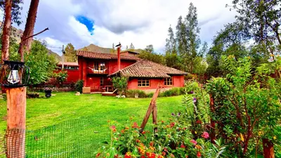 a red house with a fence in front of a yard at Casa Munay in Urubamba