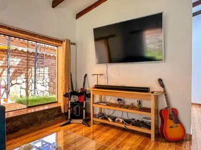 a living room with a guitar and a flat screen tv at Cancha Wasi A modern, cozy and fully equipped house in Urubamba