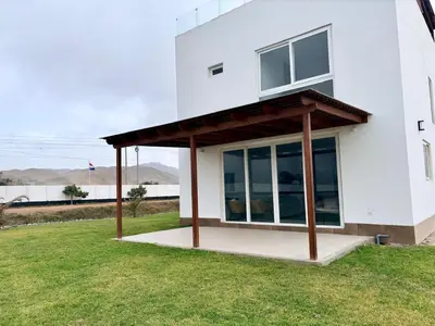 a white house with a wooden roof on a grass field at Casa de playa en Cerro Azul con piscina privada in Cerro Azul