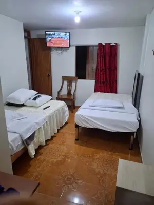 a room with two beds and a tv on the wall at Hospedaje Las Brisas in Churín