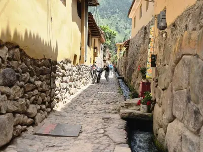 a stone alley with people walking down a street at Qhawarina Hostel Ollantaytambo in Ollantaytambo