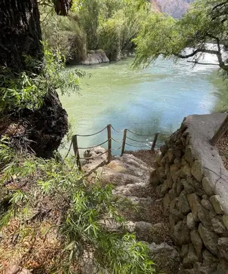 a bench next to a river with a rock wall at Tiny Mountain River in Urubamba