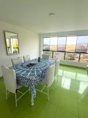 a dining room with a table with white chairs and windows at Exclusivo departamento cerca al mar in Quebrada Seca