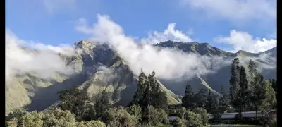 a mountain covered in clouds with trees in front of it at Florez de la Villa Apartments in Urubamba