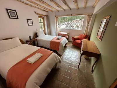 a bedroom with two beds and a chair and a window at Parwa Guest House in Ollantaytambo
