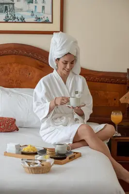 a woman sitting on a bed holding a cup of coffee at Miraflores Colon Hotel in Lima