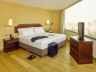 a hotel room with a bed with a television and a suitcase at Hotel Estelar Miraflores in Lima