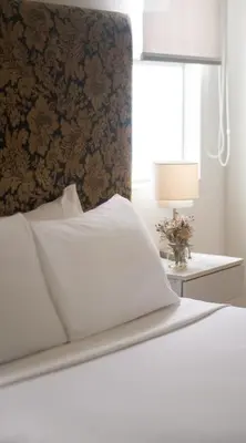 a bed with white sheets and a wall with a window at El Golf Hotel Boutique in Lima