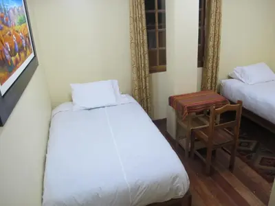 a room with two beds and a chair and a table at Tumy house B&B in Ollantaytambo
