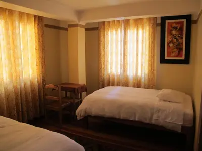 a bedroom with two beds and a chair and curtains at Tumy house B&B in Ollantaytambo