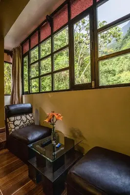 a living room with a couch and a table and windows at Samananchis Machupicchu in Machu Picchu