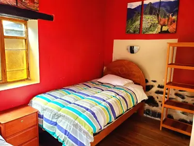 a bedroom with a bed in a red wall at Hospedaje K'uchuwasi in Ollantaytambo