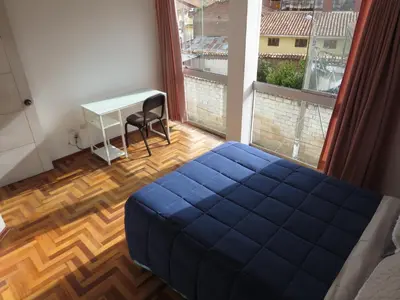 a bedroom with a blue bed and a desk and a window at Apartamentos Quewe in Cusco