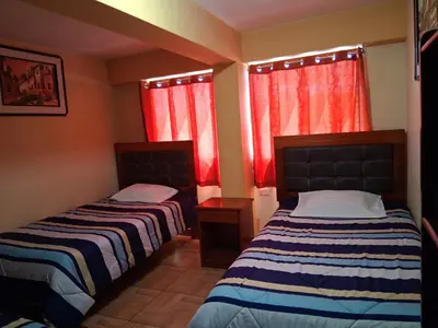 two beds in a room with red curtains at Hostal Kuntur Cusco in Cusco